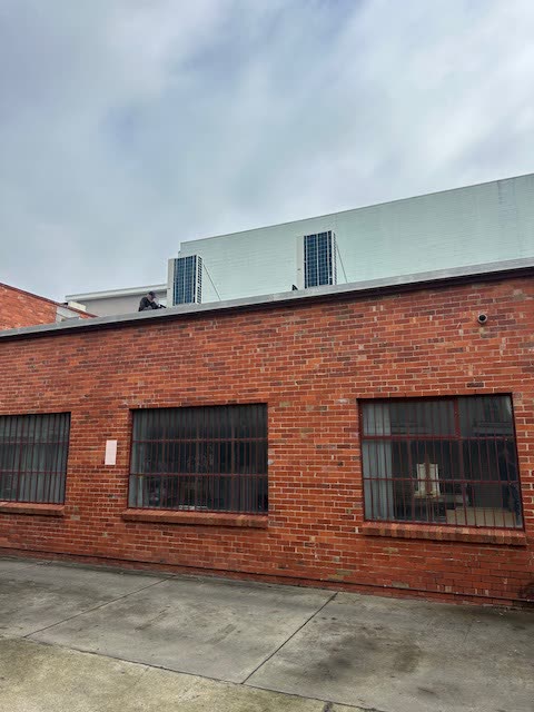 Outdoor condensing units installed on the roof of a red brick commercial building.