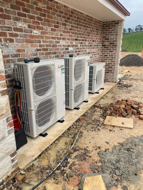 Three Mitsubishi Electric outdoor condensing units installed in a row beside a new build.