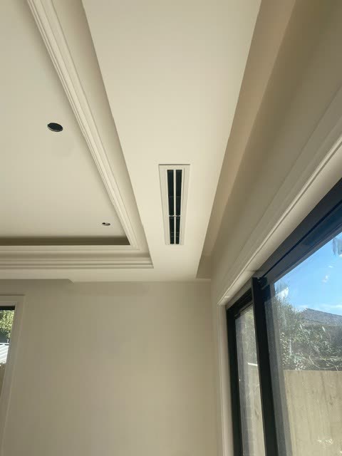 Linear slot diffuser set into a ceiling beside ornate cornice work.