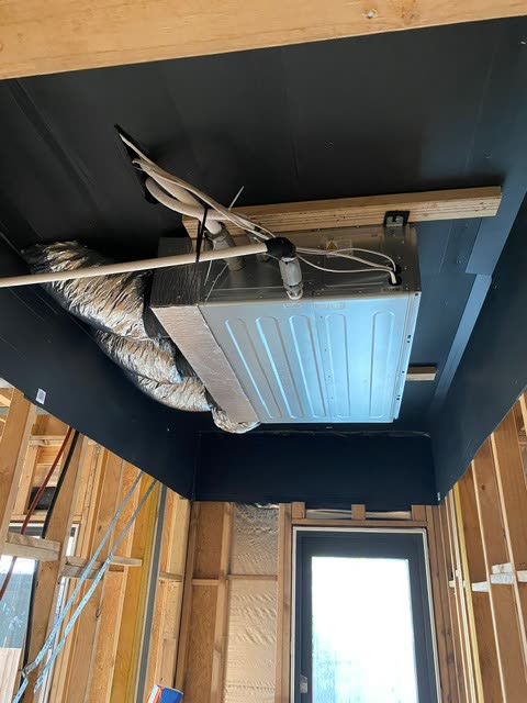 Indoor fan coil unit installed inside a dark painted ceiling bulkhead with insulated flexible duct connected.