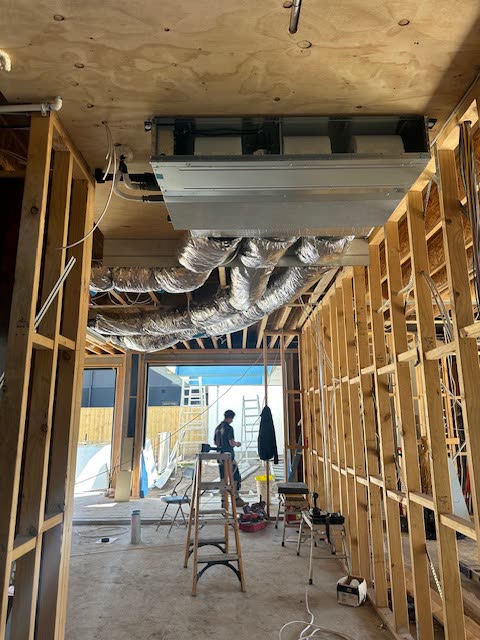 Ducted fan coil fixed under a plywood ceiling in a timber framed extension, insulated flexible ducts running out from it.
