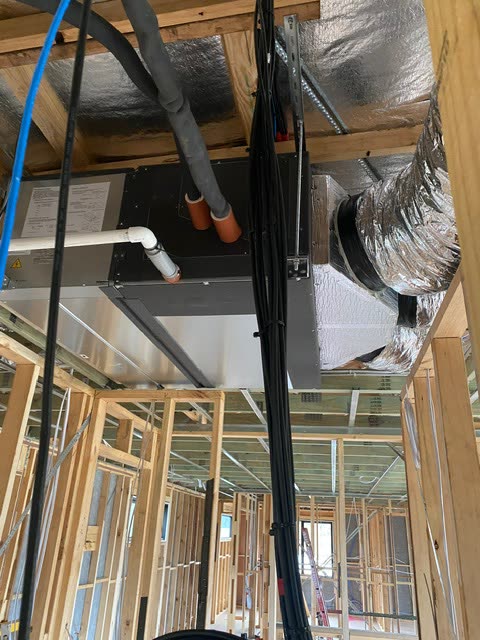 Ducted fan coil unit suspended in the roof space of a timber framed house, with lagged refrigerant lines and a condensate drain connected.