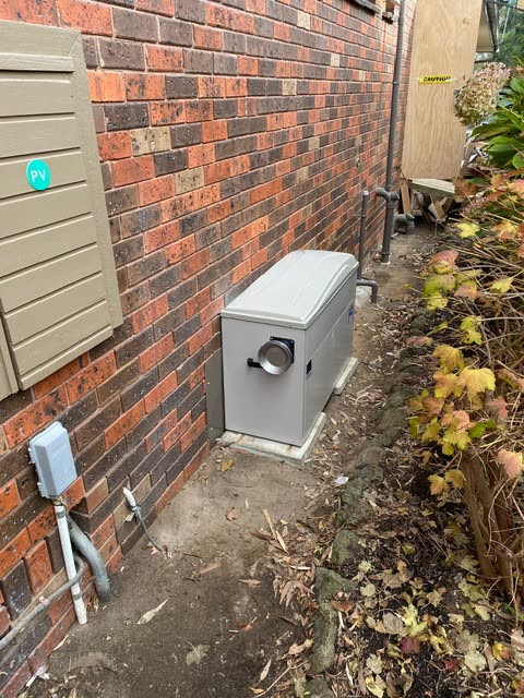 External gas ducted heater unit installed against the side of a brick house.