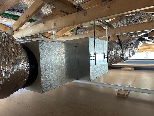 Galvanised plenum box installed under roof trusses with insulated flexible ducts branching off it.