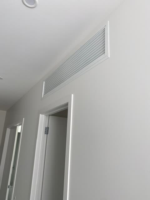 Linear bar return air grille set into a hallway wall near the ceiling in a finished white interior.