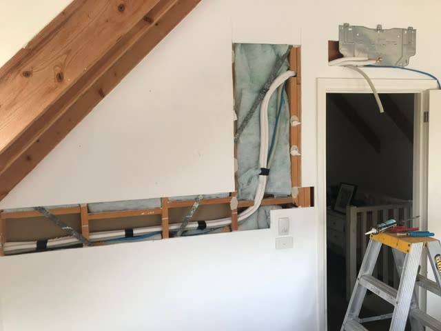 Upstairs bedroom wall opened up, plasterboard cut away to show insulation, framing and the pipework run, with the mounting plate fixed above the doorway.