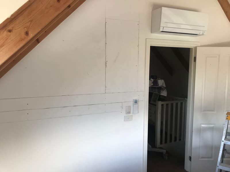 The same wall finished, with the split system head unit installed above the doorway and the remote mounted beside the light switch.