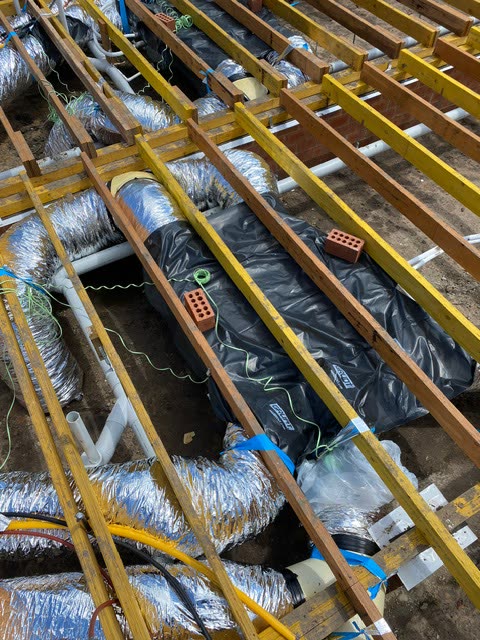Insulated flexible ducting and a flat plenum run between floor joists in a subfloor, before the flooring goes down.